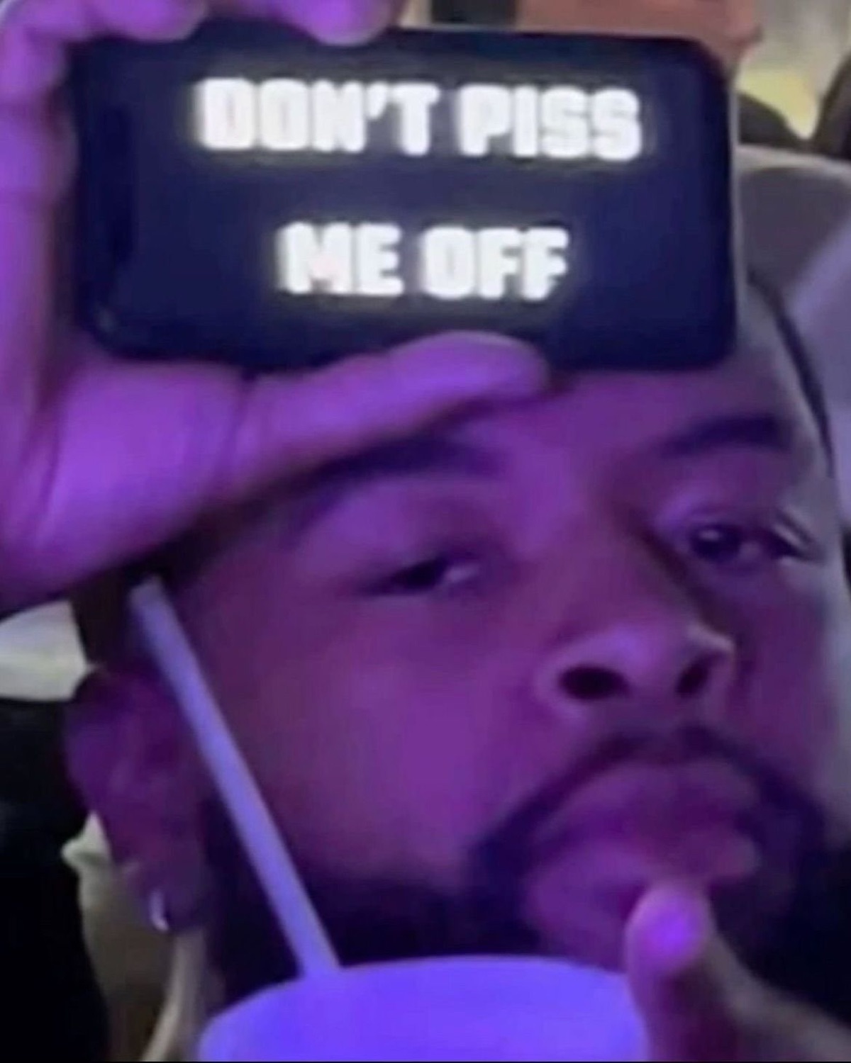 Man holding a phone to his forehead reading 'DON'T PISS ME OFF' with a deadpan glare