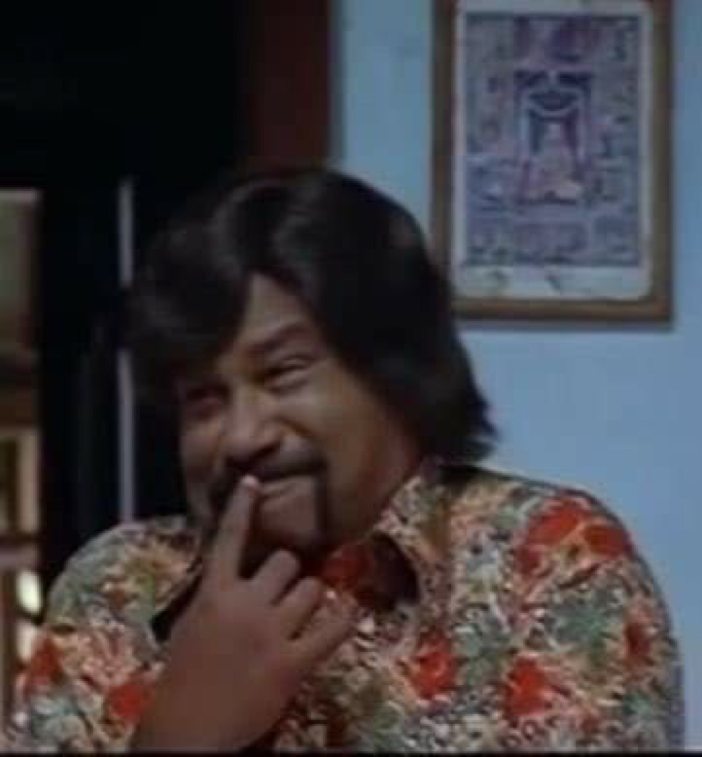Man in a floral shirt with a shy finger-to-lip smile