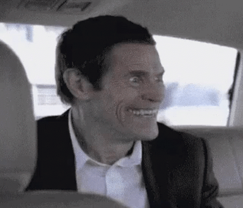 Willem Dafoe turning to the camera with an unhinged wide grin