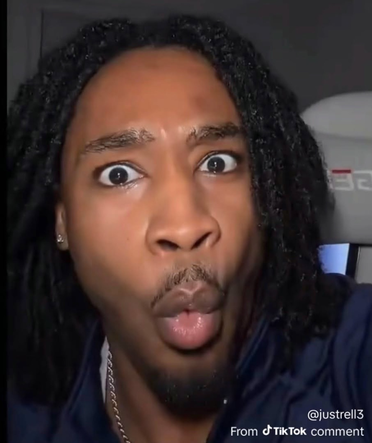 Man with locs in a car staring wide-eyed into the camera with lips slightly parted