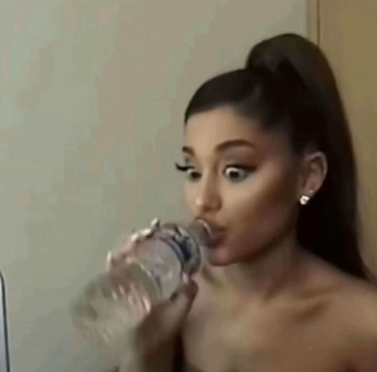 Woman with a high ponytail drinking water and looking startled mid-sip