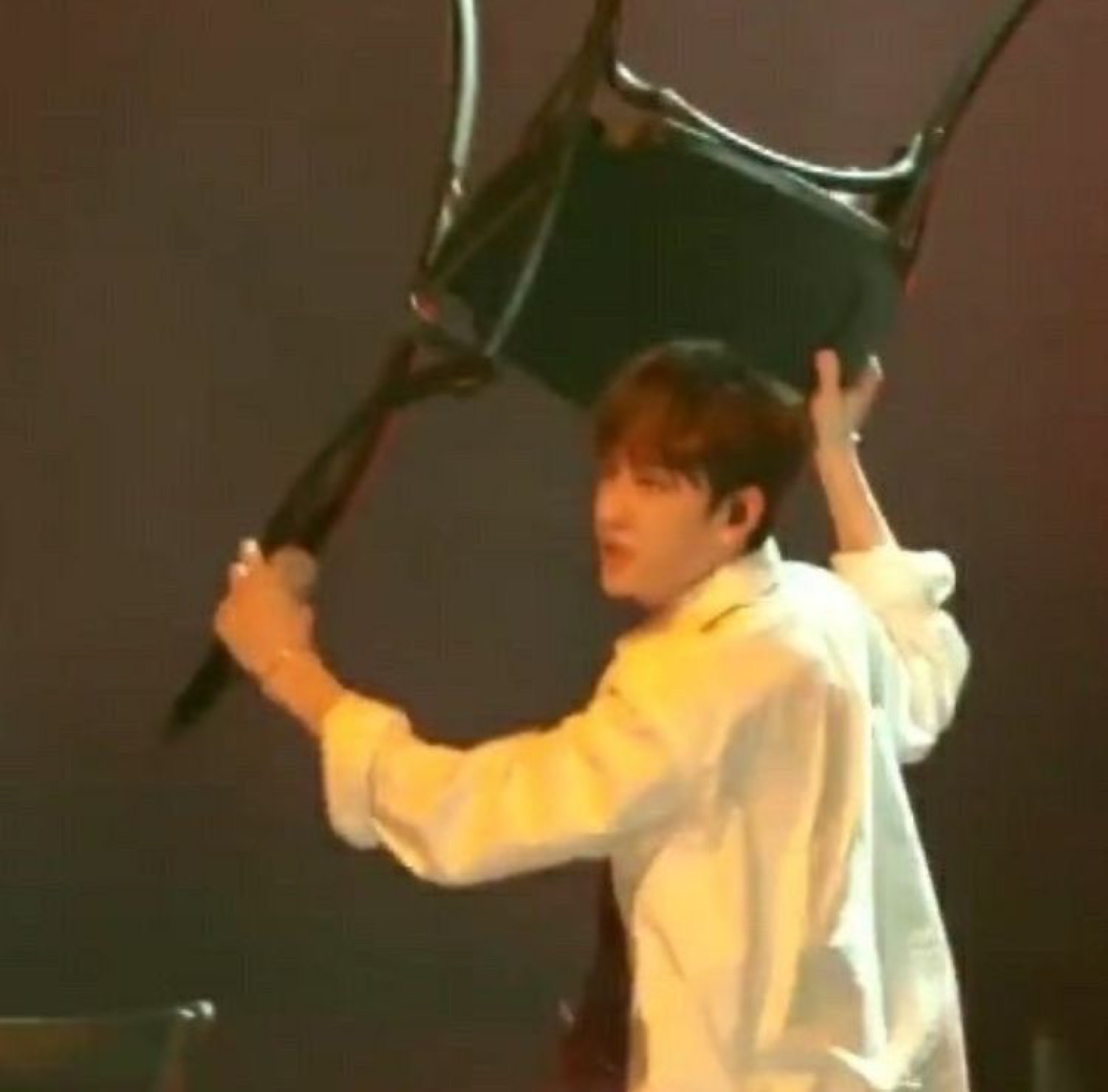 Young man on stage dramatically hoisting a chair over his head