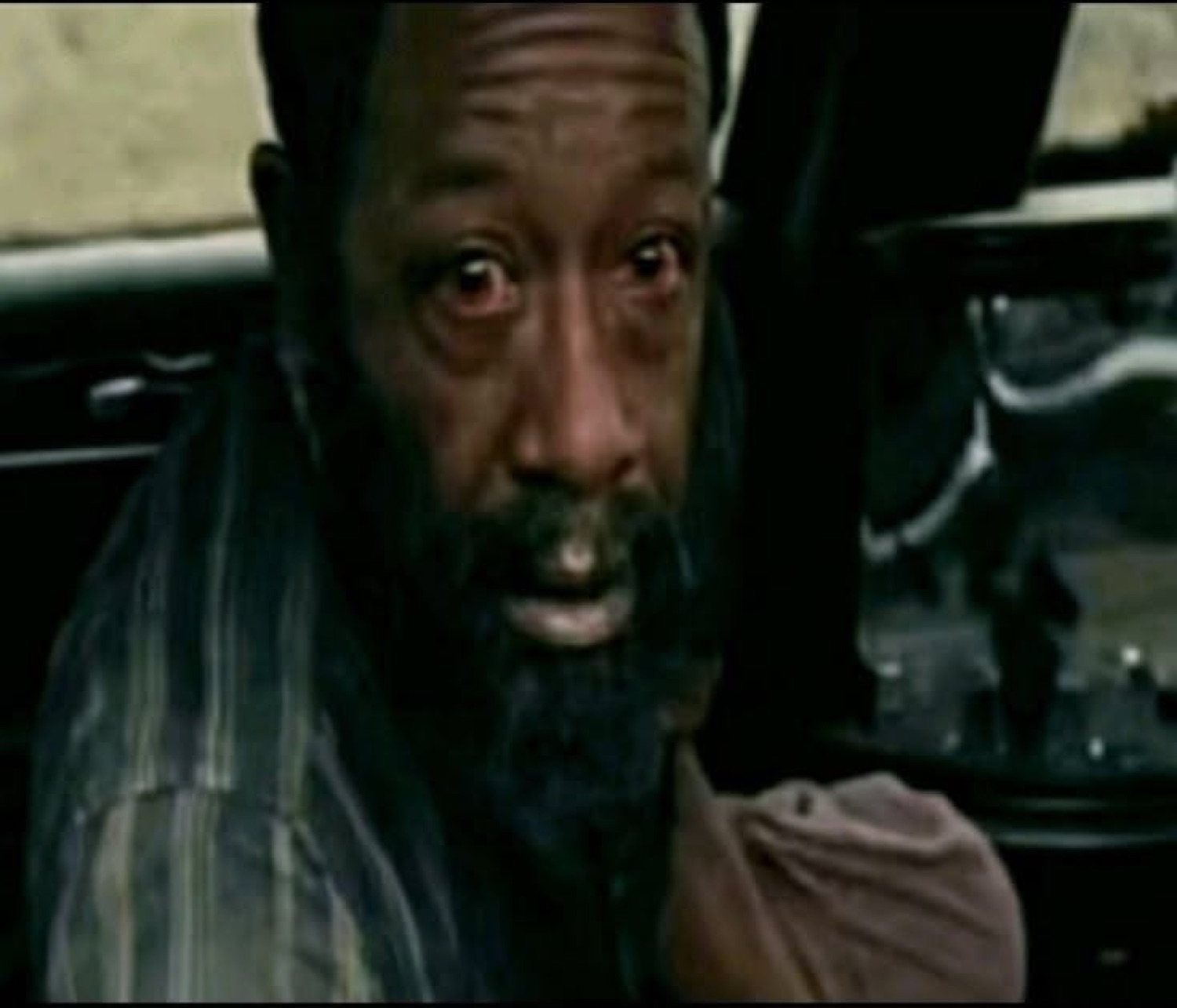 Older bearded man in a car with red, teary eyes and a heartbroken stare