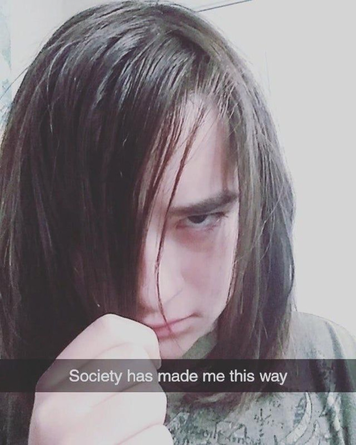 Long-haired teen glaring through their fringe captioned 'Society has made me this way'