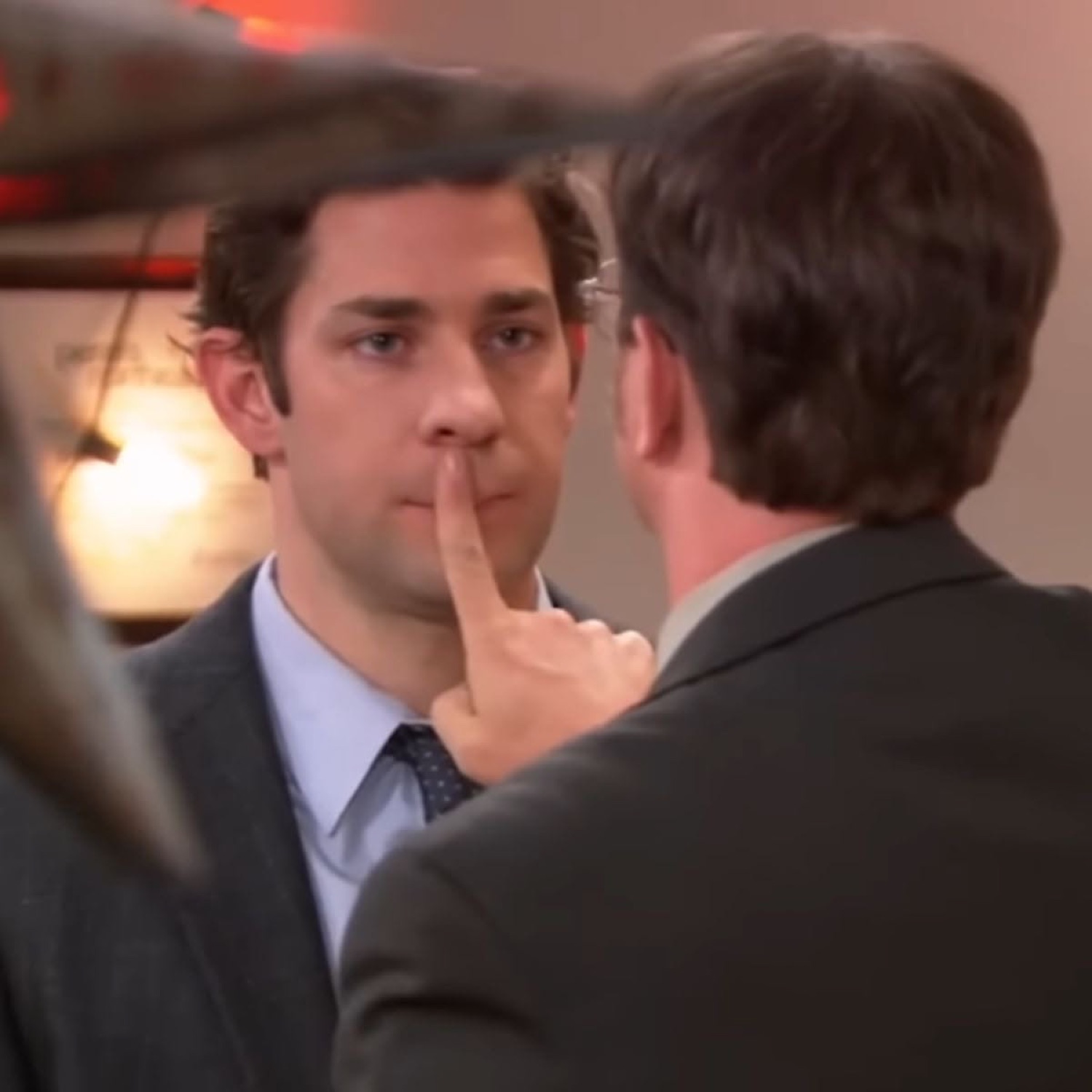 Jim from The Office shushing Dwight with a finger to his lips