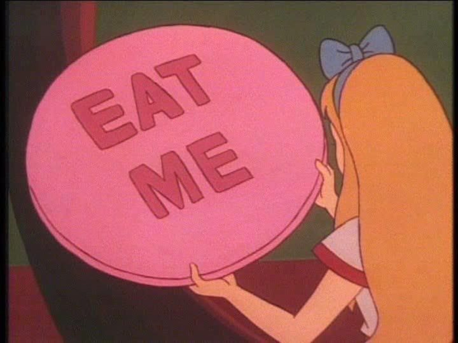 Alice holding up the giant pink 'EAT ME' cake with both hands