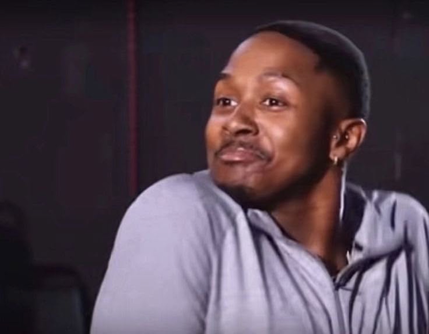 Man in gray hoodie casting a knowing smug side glance off camera