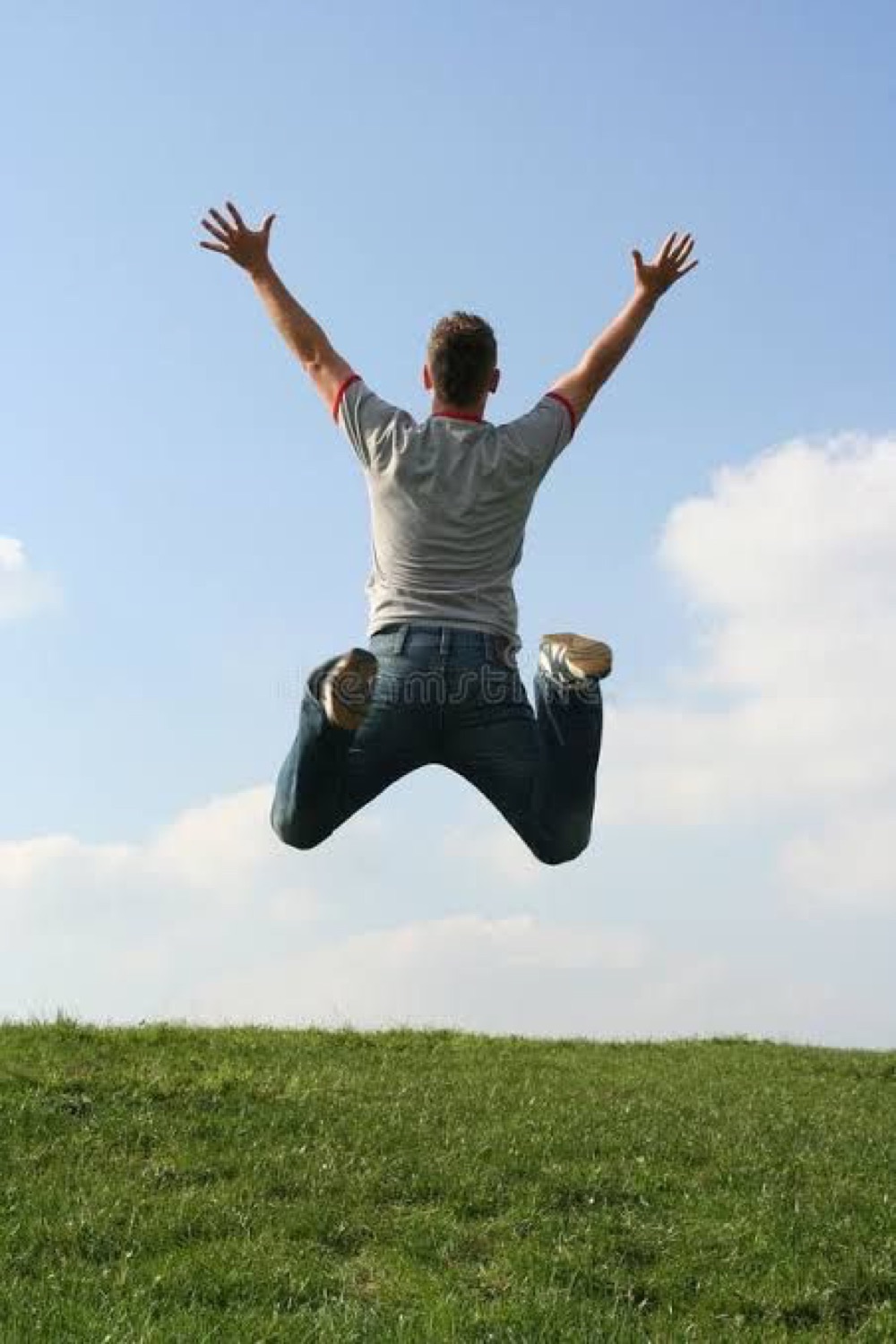 Man leaping into the air on a grassy hill with arms stretched wide