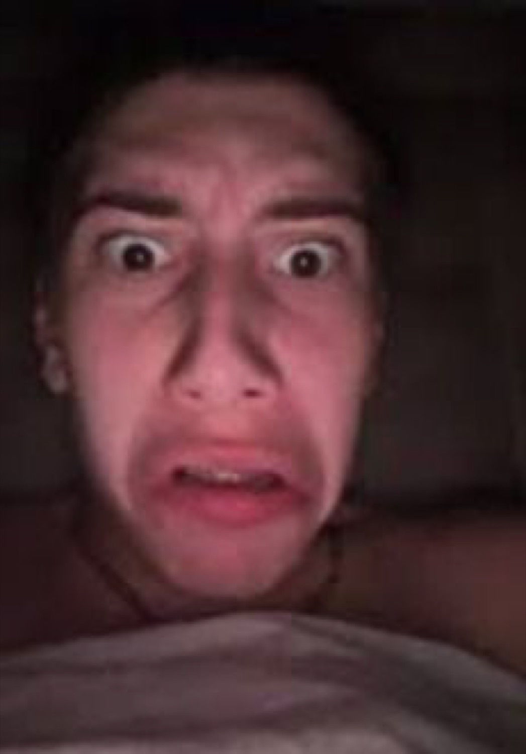 Person in the dark with wide eyes and gritted teeth in total terror