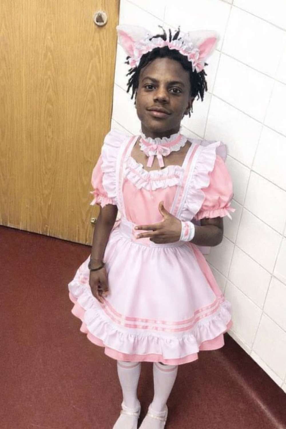 Person in a frilly pink lolita dress and bunny-ear headband posing stiffly in a hallway