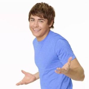 Young man in a blue tee grinning and gesturing with both open hands like 'ta-da'