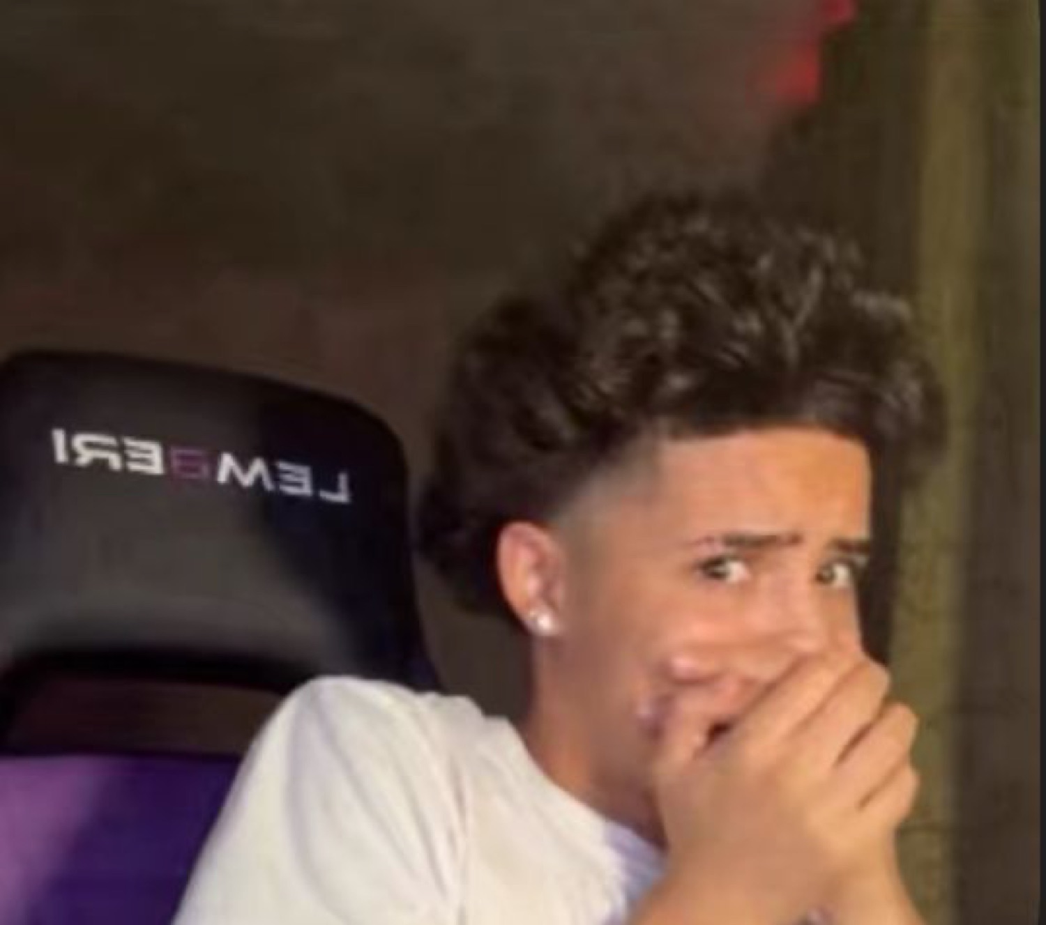 Young man at a gaming chair covering his mouth in horror