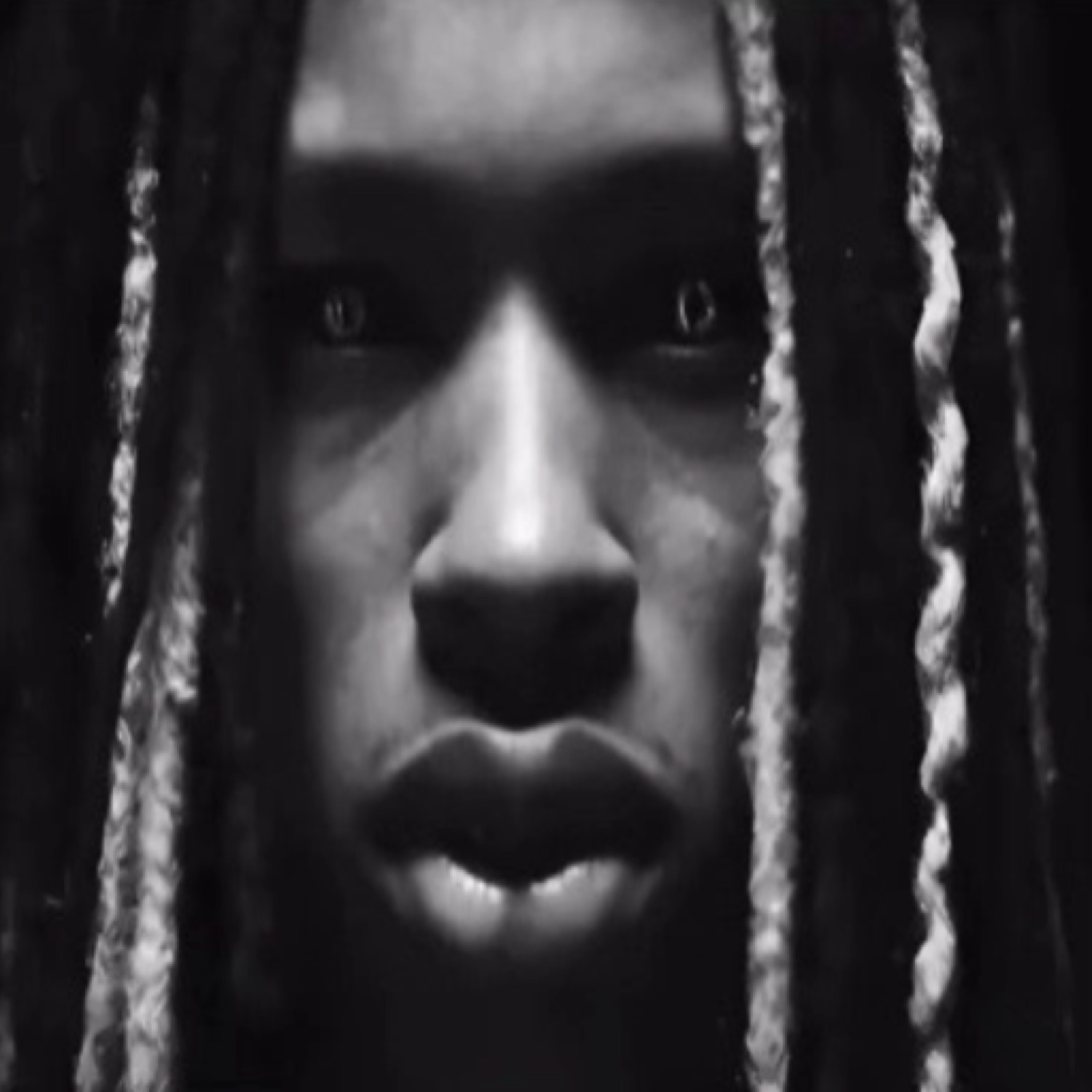 Man with locs staring intensely through the dark in a black-and-white close-up