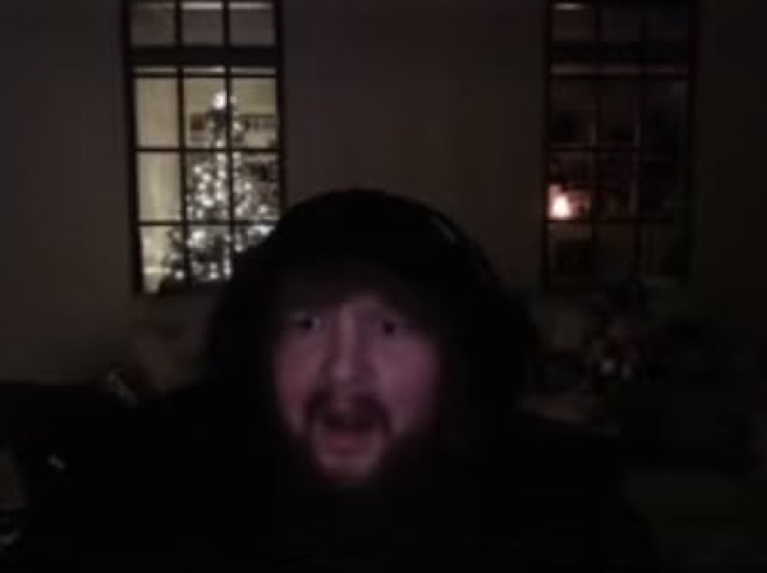 Guy in a hood on a dark webcam, unimpressed with holiday lights behind him