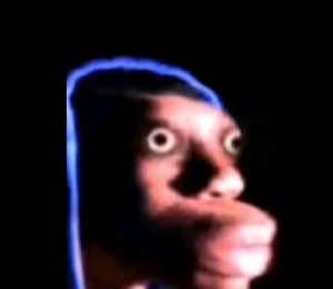 Person in a hoodie with wide terrified eyes lit up in the dark