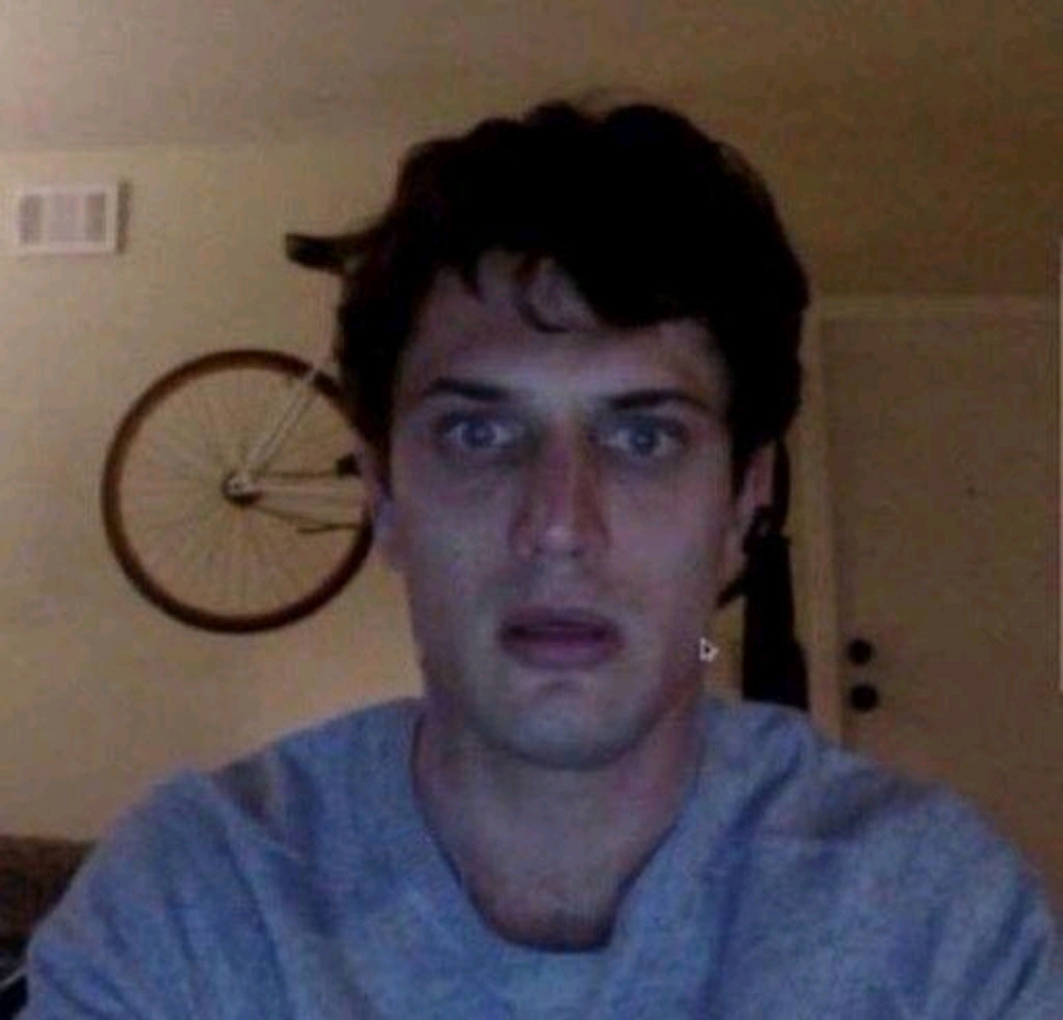 Man on a dim webcam staring blankly with a stunned, hollow look