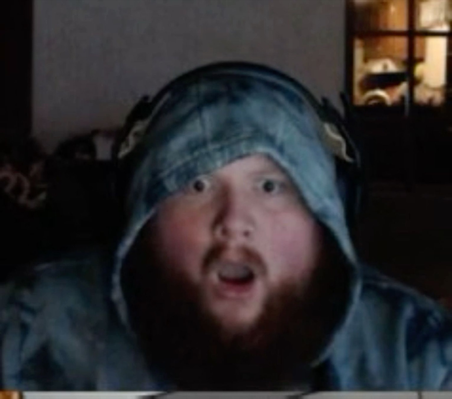 Bearded man in a backwards denim cap gaping wide-eyed at his screen
