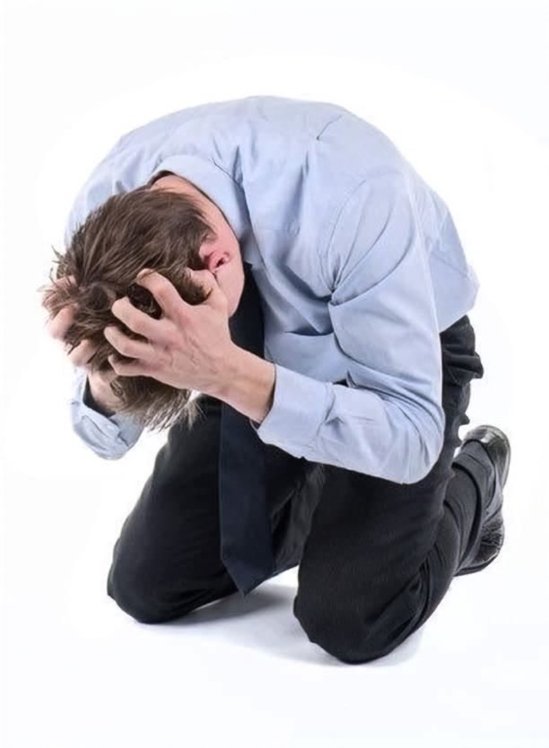 Man in a dress shirt kneeling on the floor with his head buried in his hands in total breakdown