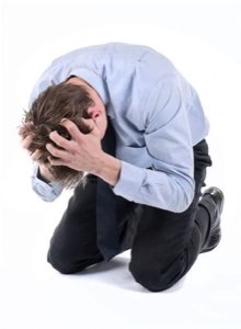 Man in a dress shirt kneeling on the floor with his head buried in his hands in total breakdown