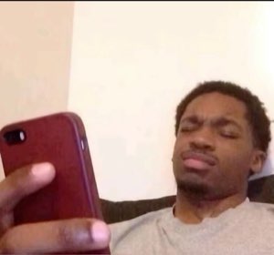 Guy lying on a couch barely looking up from his phone with heavy lidded eyes