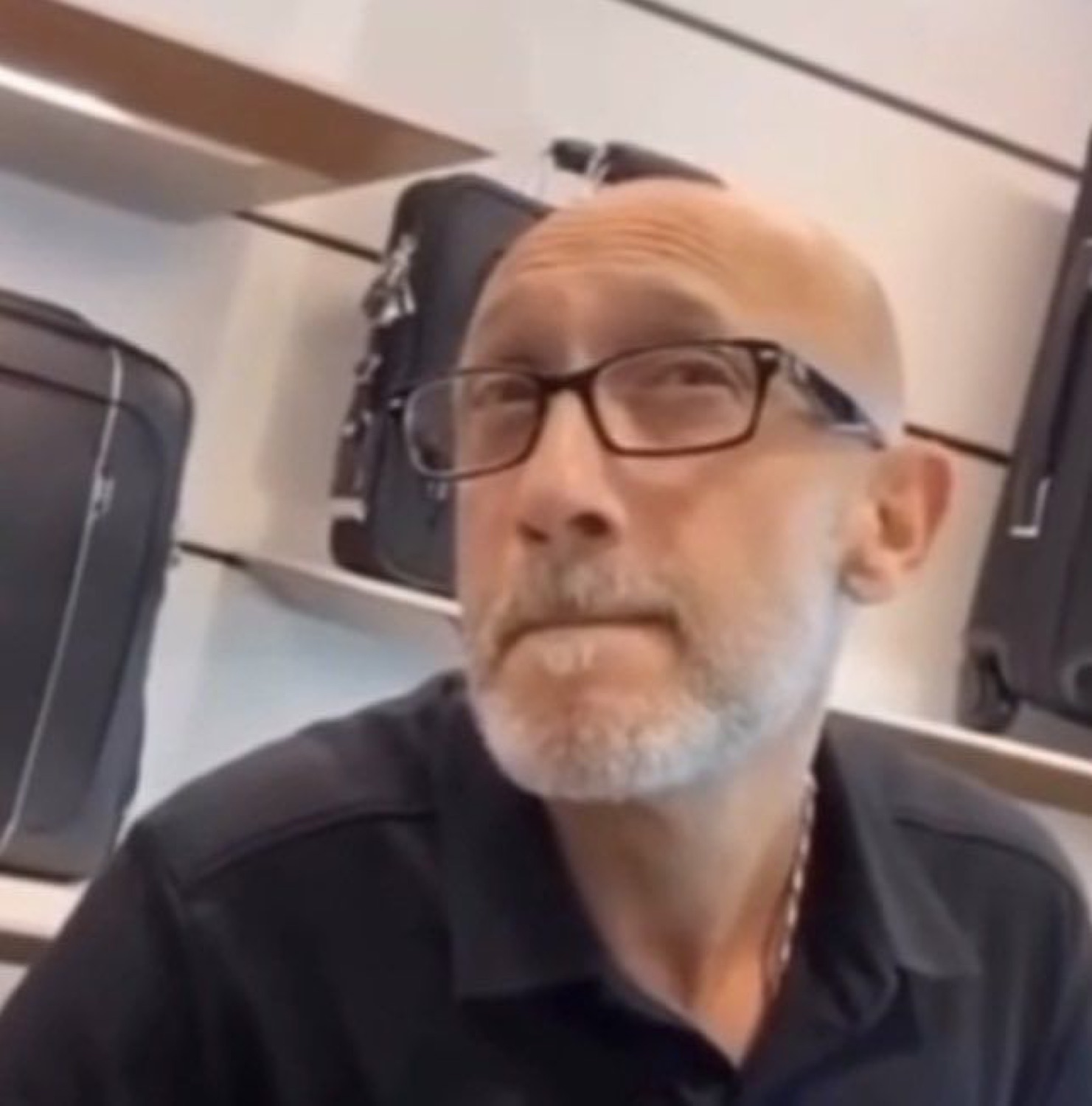 Bald man with glasses looking sideways with the flattest, most unreadable expression