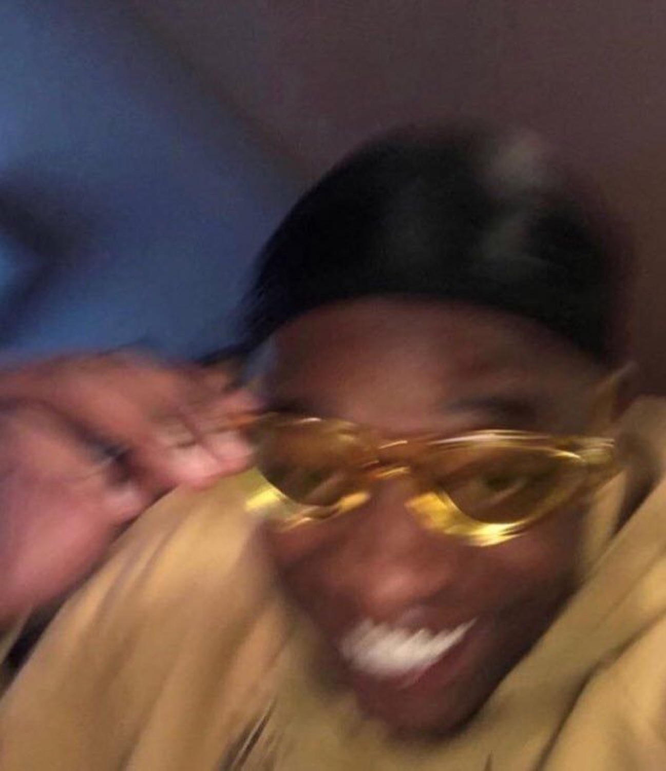 Man in gold glasses grinning in a blur