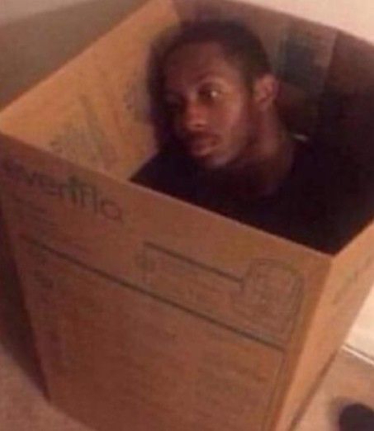 Man crouched inside a cardboard box peeking out with a caught, wide-eyed stare