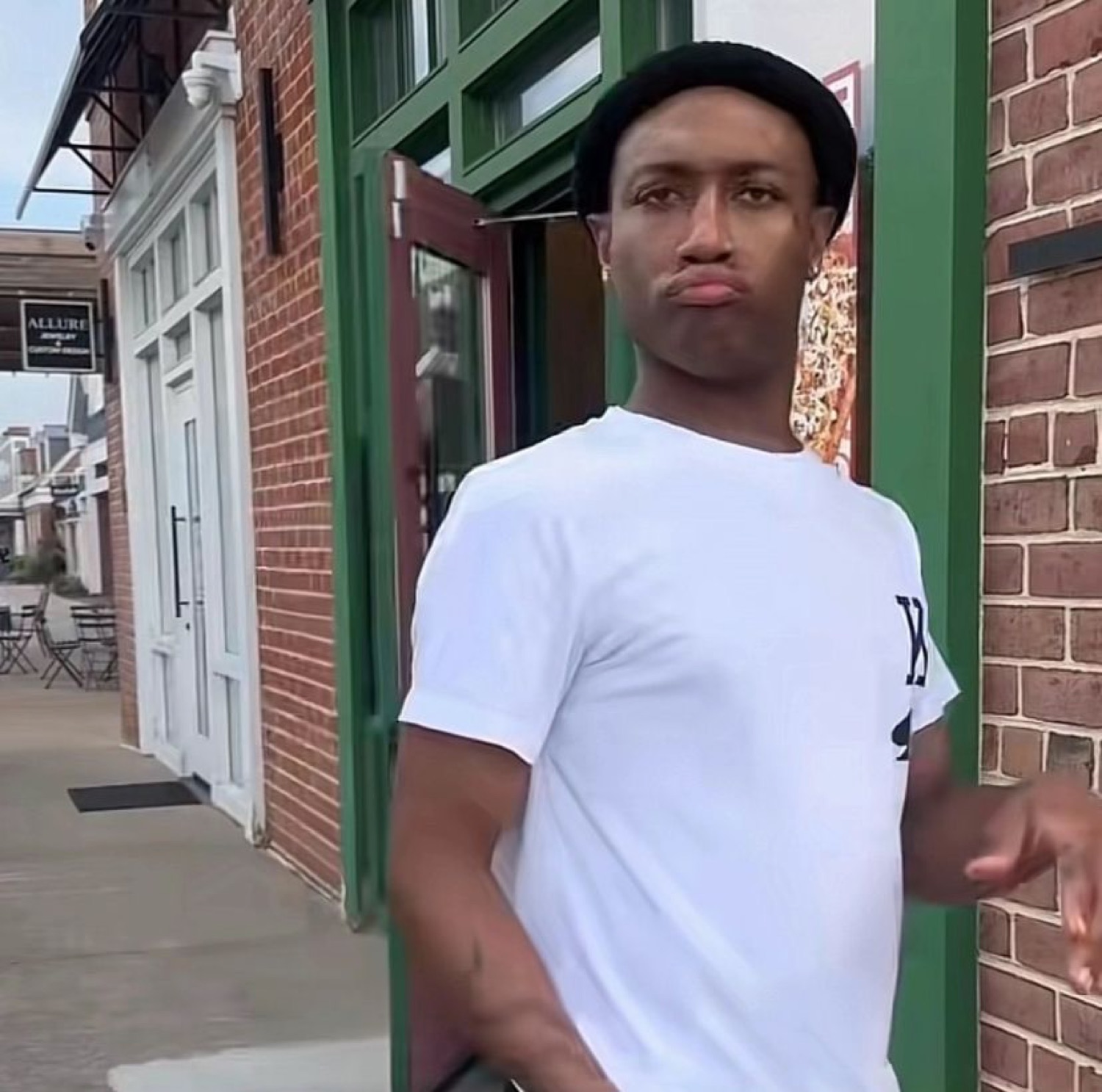 Guy in a beanie and white tee posing outside a storefront with a cool, unbothered pout