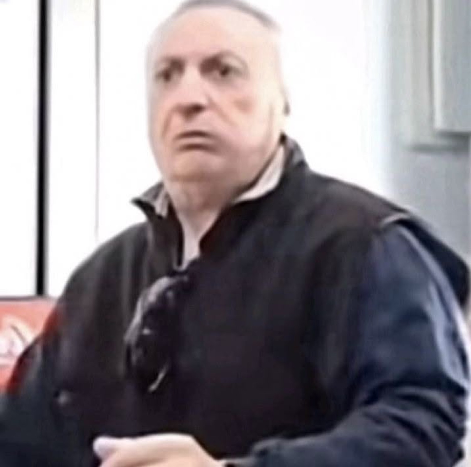 Older man in a vest giving a skeptical, unimpressed frown across the room