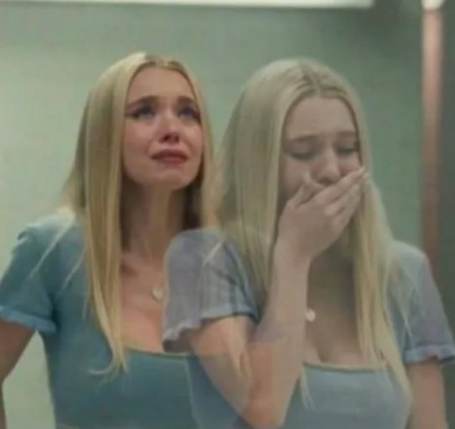 Two blonde girls in matching blue dresses tearing up, one covering her mouth in shock
