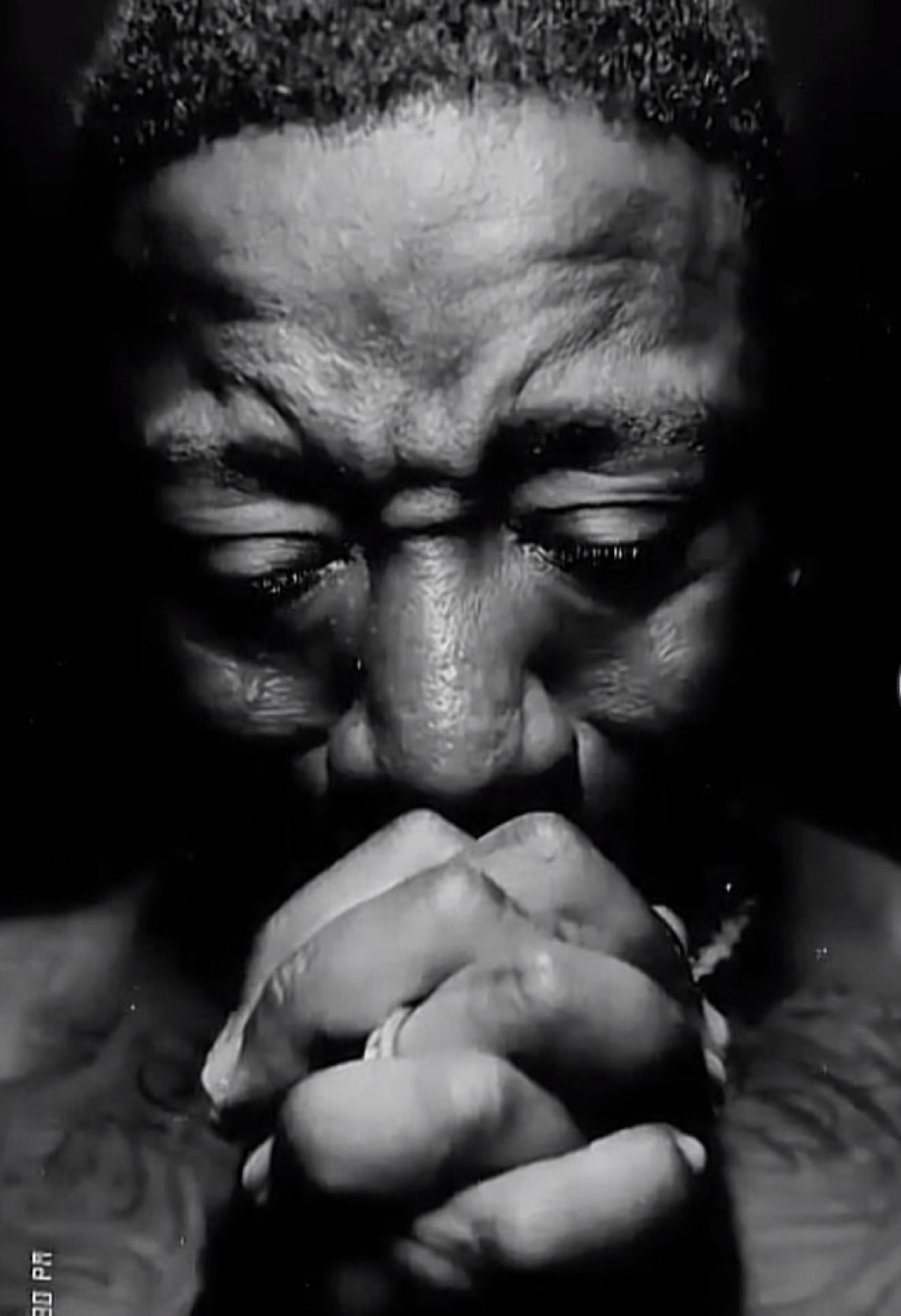 Man with eyes closed and hands clasped tightly in prayer, shot in dramatic black and white
