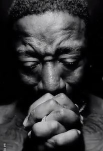 Man with eyes closed and hands clasped tightly in prayer, shot in dramatic black and white
