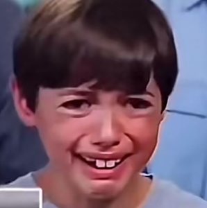 Young boy with a scrunched face fighting back tears and a shaky forced smile