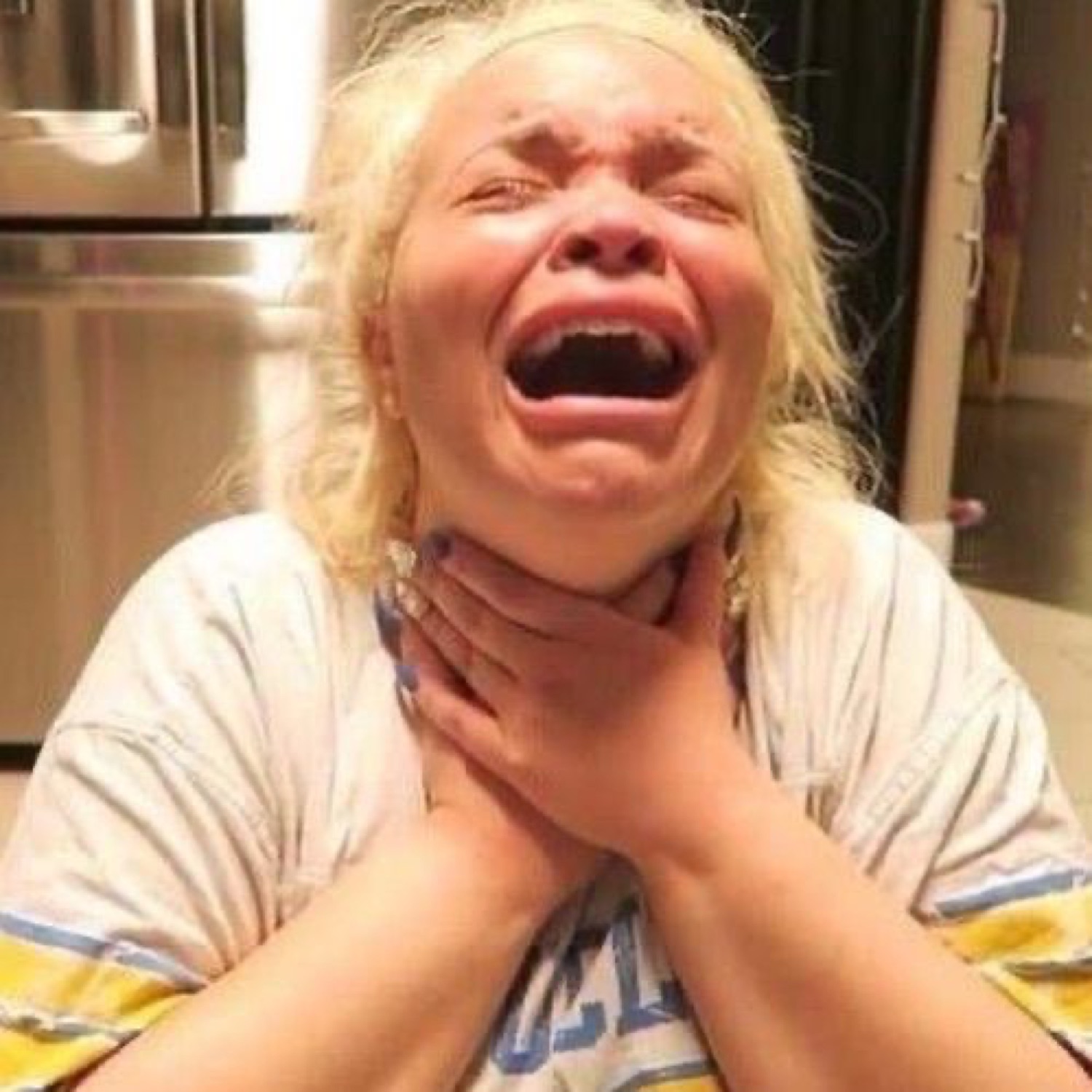 Blond woman wailing and clutching her own throat in absolute anguish in a kitchen