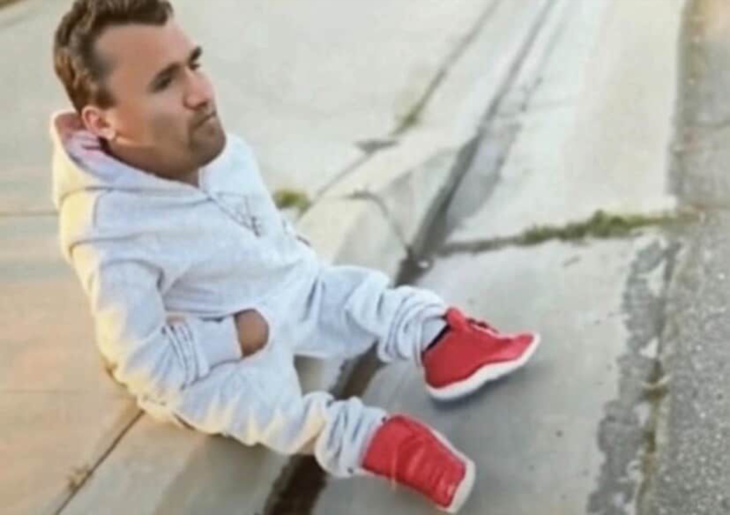 Guy in a grey hoodie and red sneakers lounging on a curb, staring into nothing
