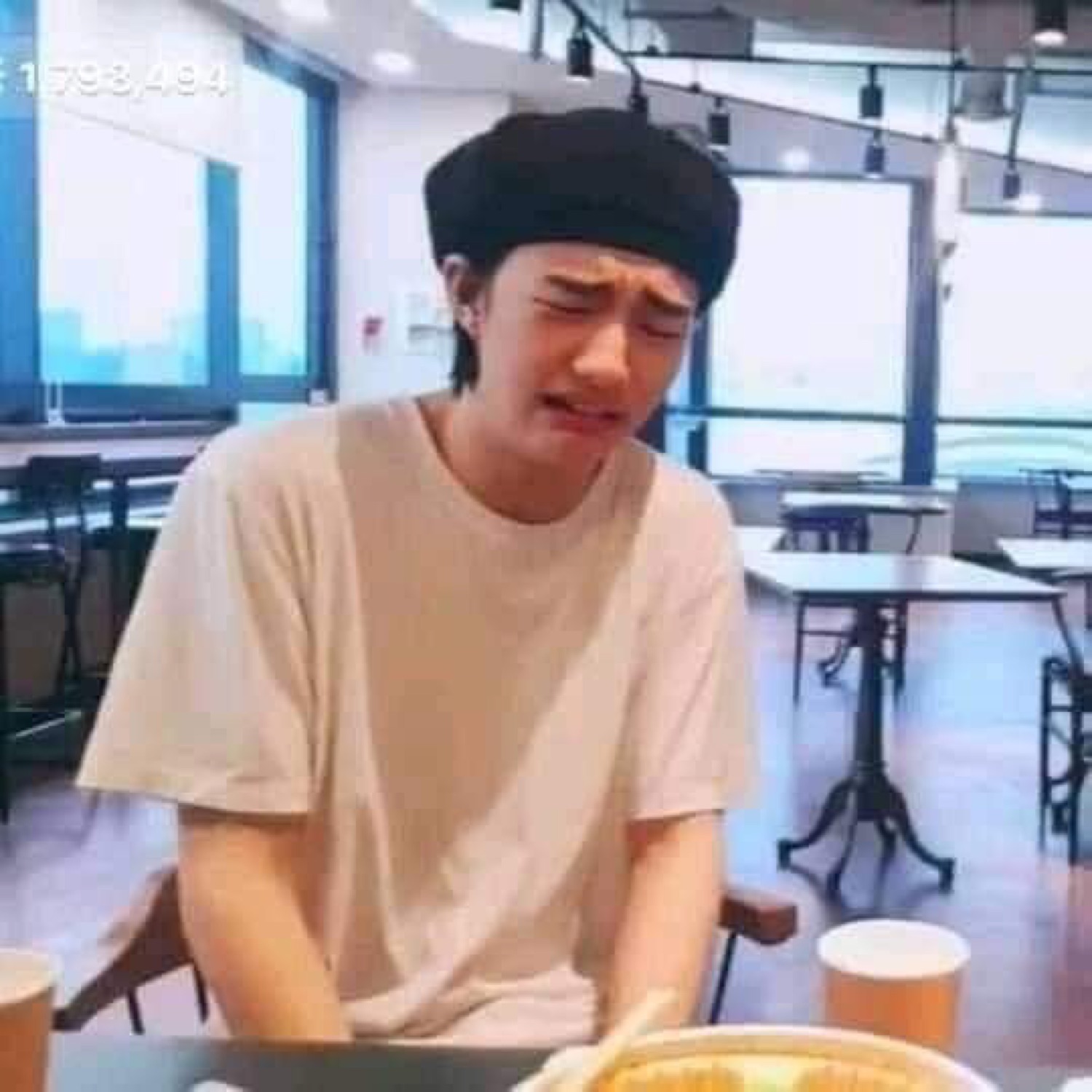Young man in a beret at a table wincing and crying over his food