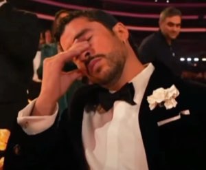 Man in a tuxedo at an awards show rubbing his face with his hand in exhausted disbelief