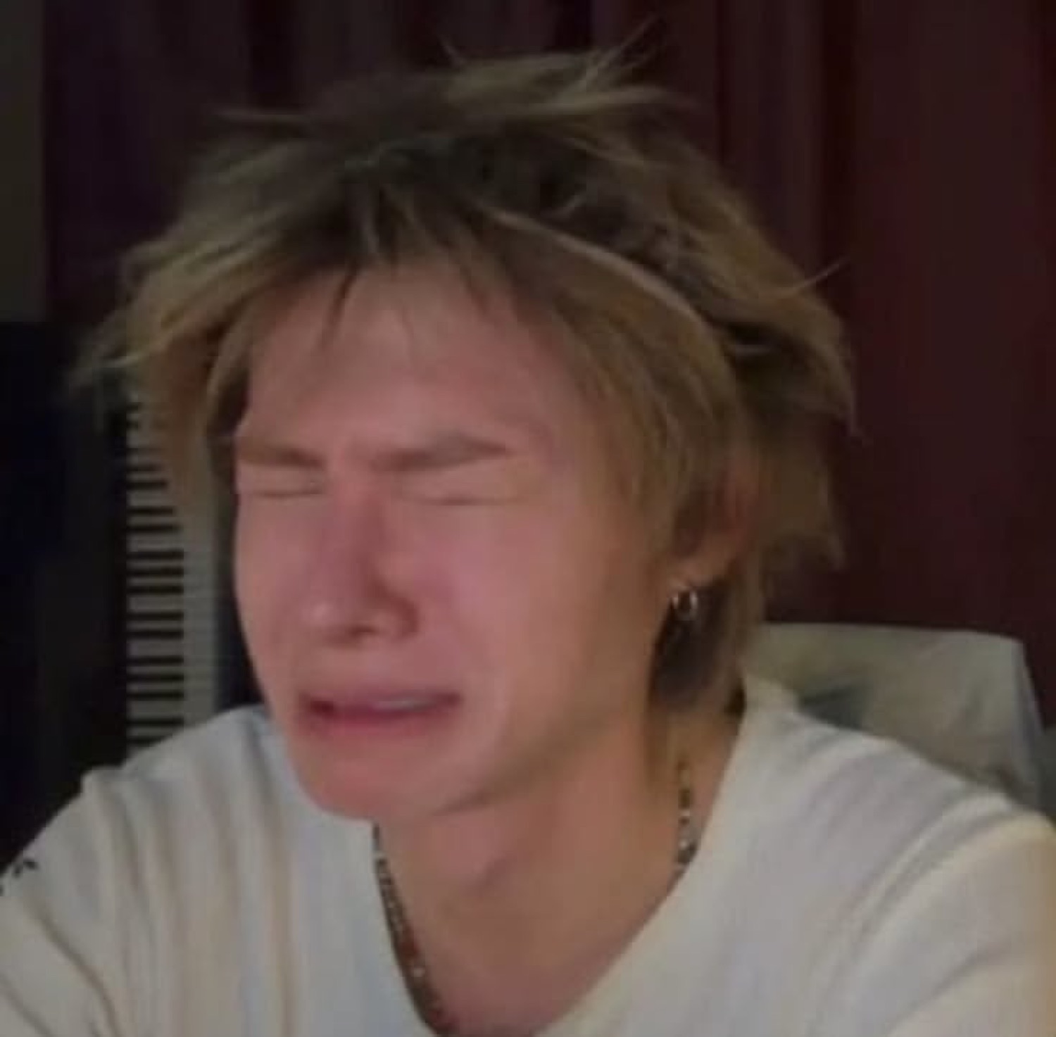 Person with messy blond hair crying with eyes shut tight on a live stream