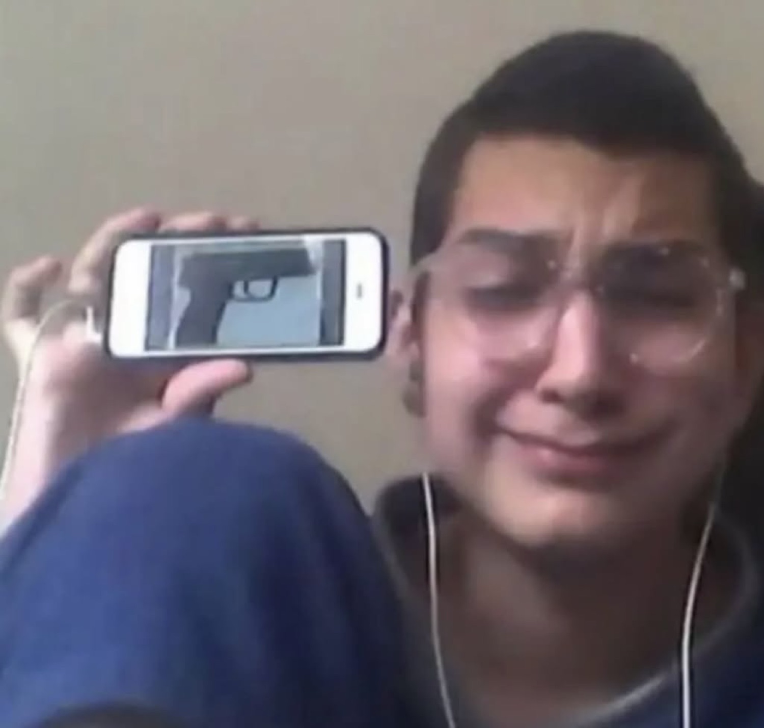 Teenager crying while holding up a phone showing a picture of a gun to the camera