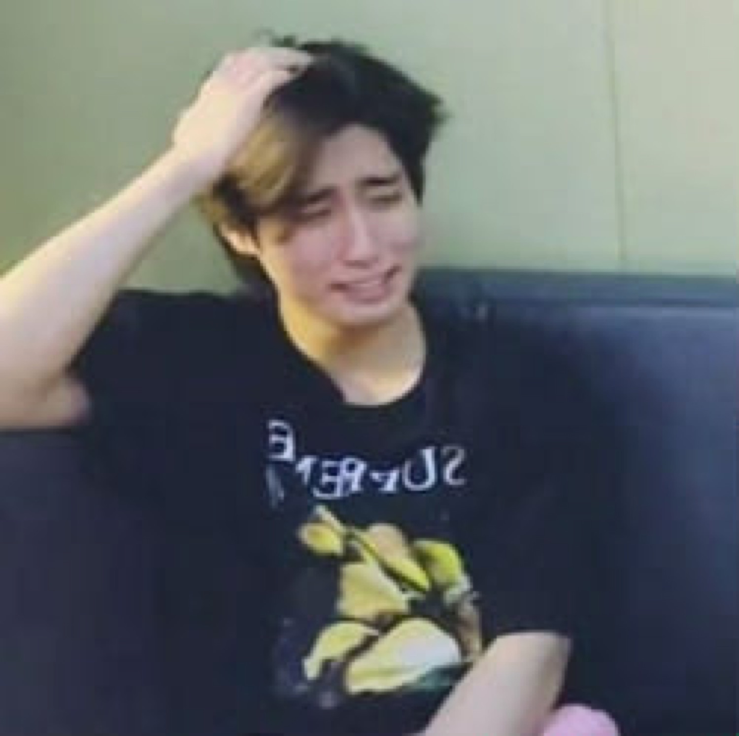 Young man crying and grabbing his hair while sitting on a couch, visibly distressed