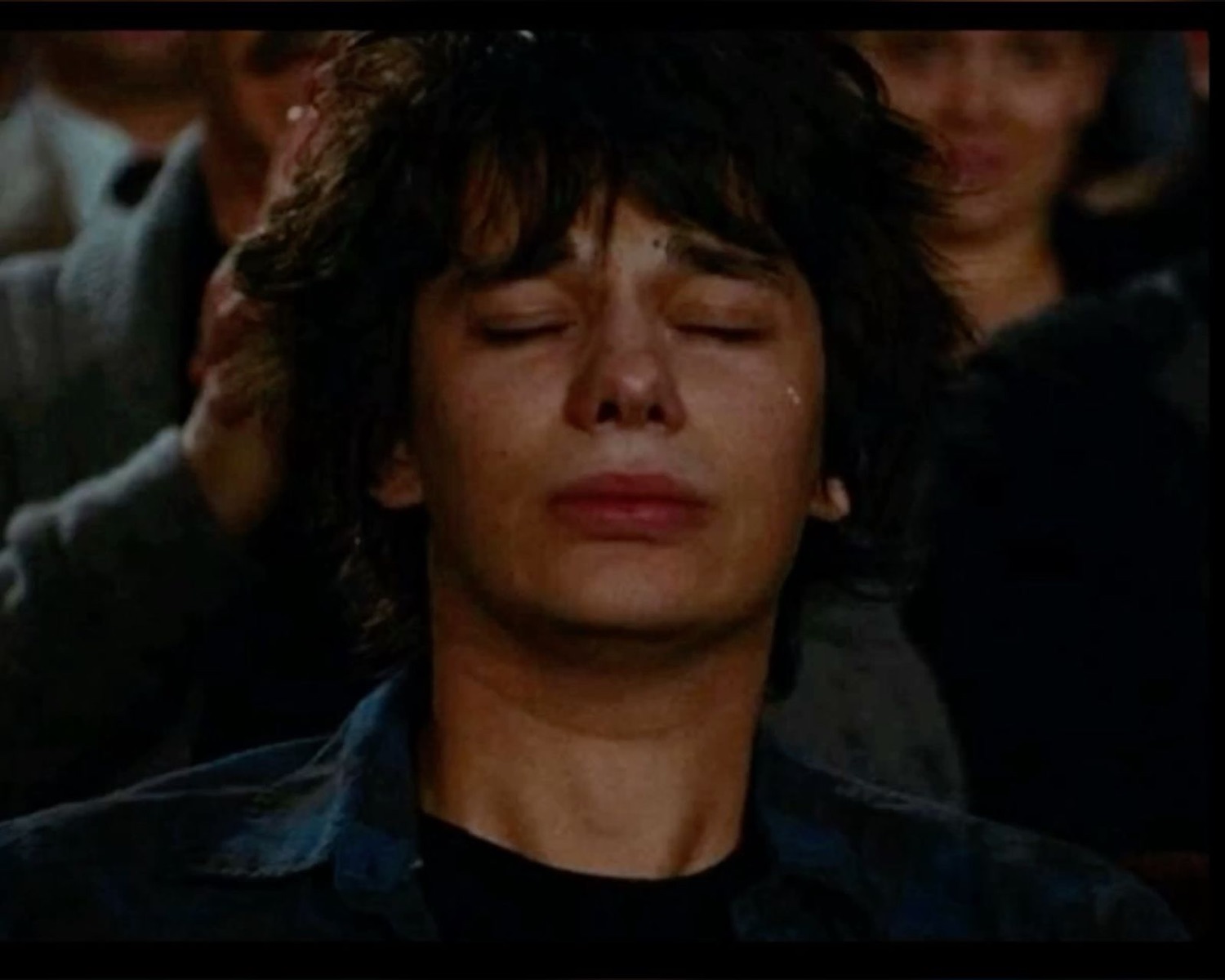 Young man with eyes closed, tears rolling down, totally overcome with emotion in a crowd