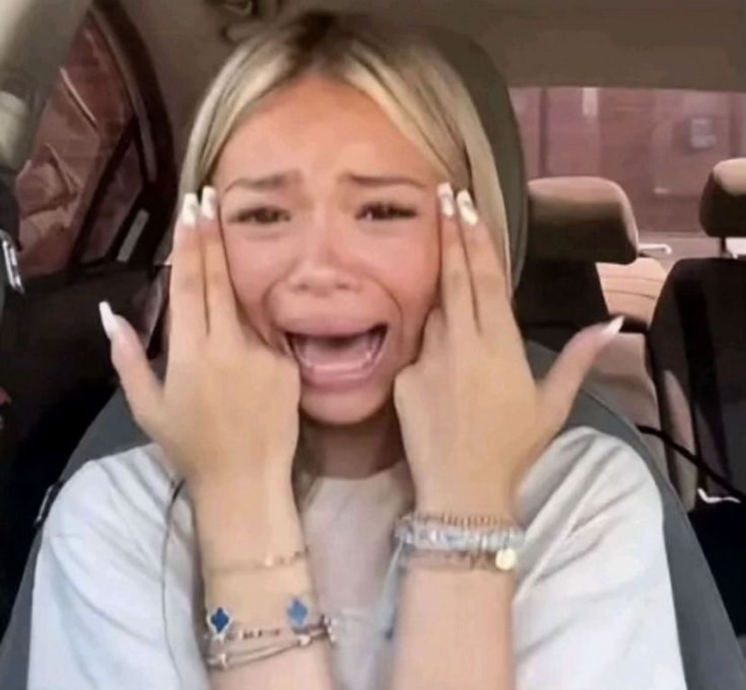 Blonde woman sobbing with hands to her face in the car