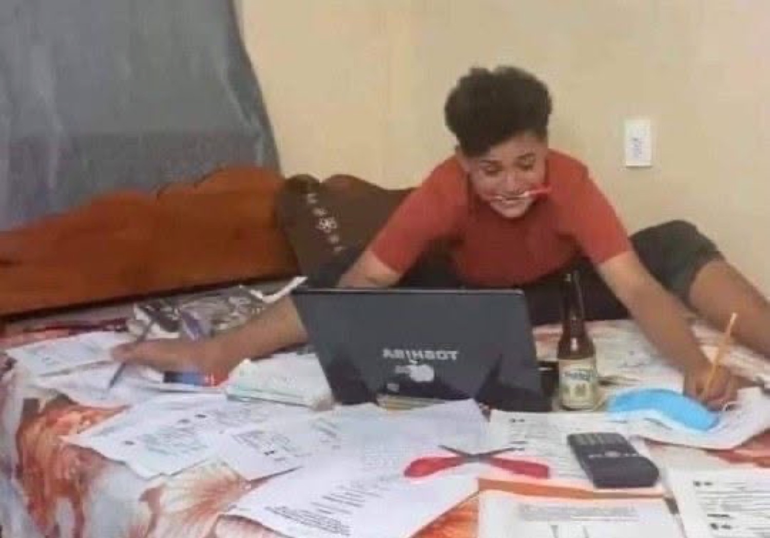 Guy grinning while sprawled across a bed buried in papers and a laptop