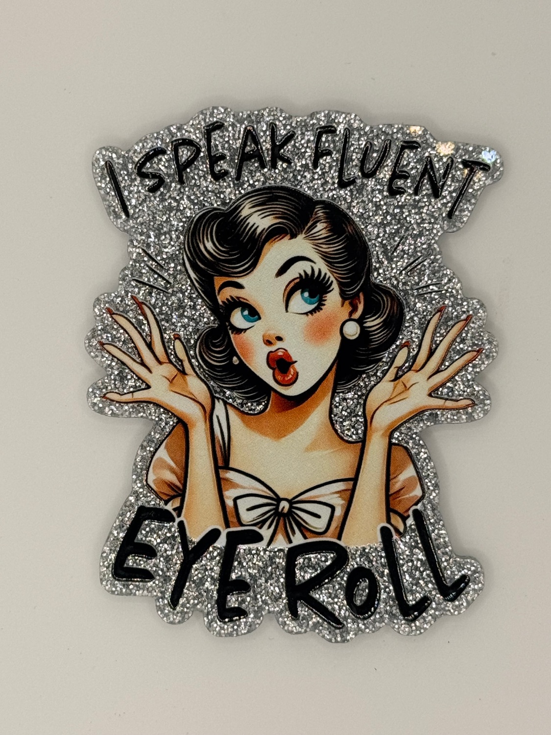 Glittery pin-up sticker of a wide-eyed woman, captioned 'I speak fluent eye roll'