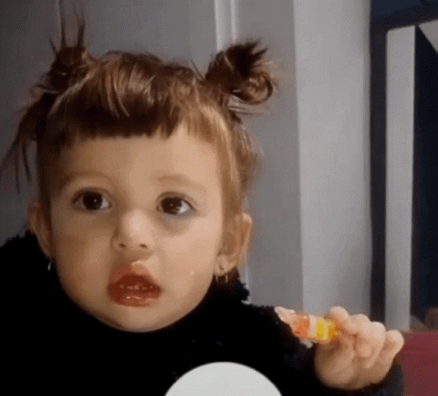 Toddler with space buns holding a snack and staring blankly with her mouth slightly open