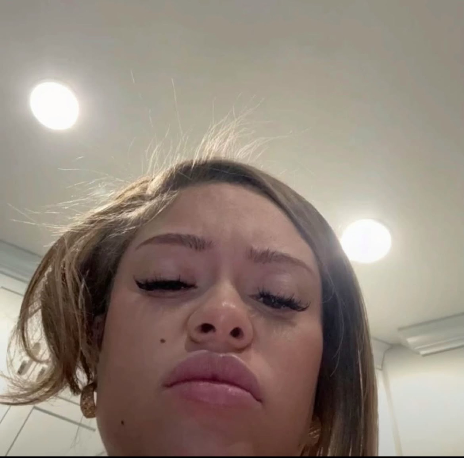 Low-angle selfie of a woman with heavy-lidded eyes and a flat, thoroughly done expression