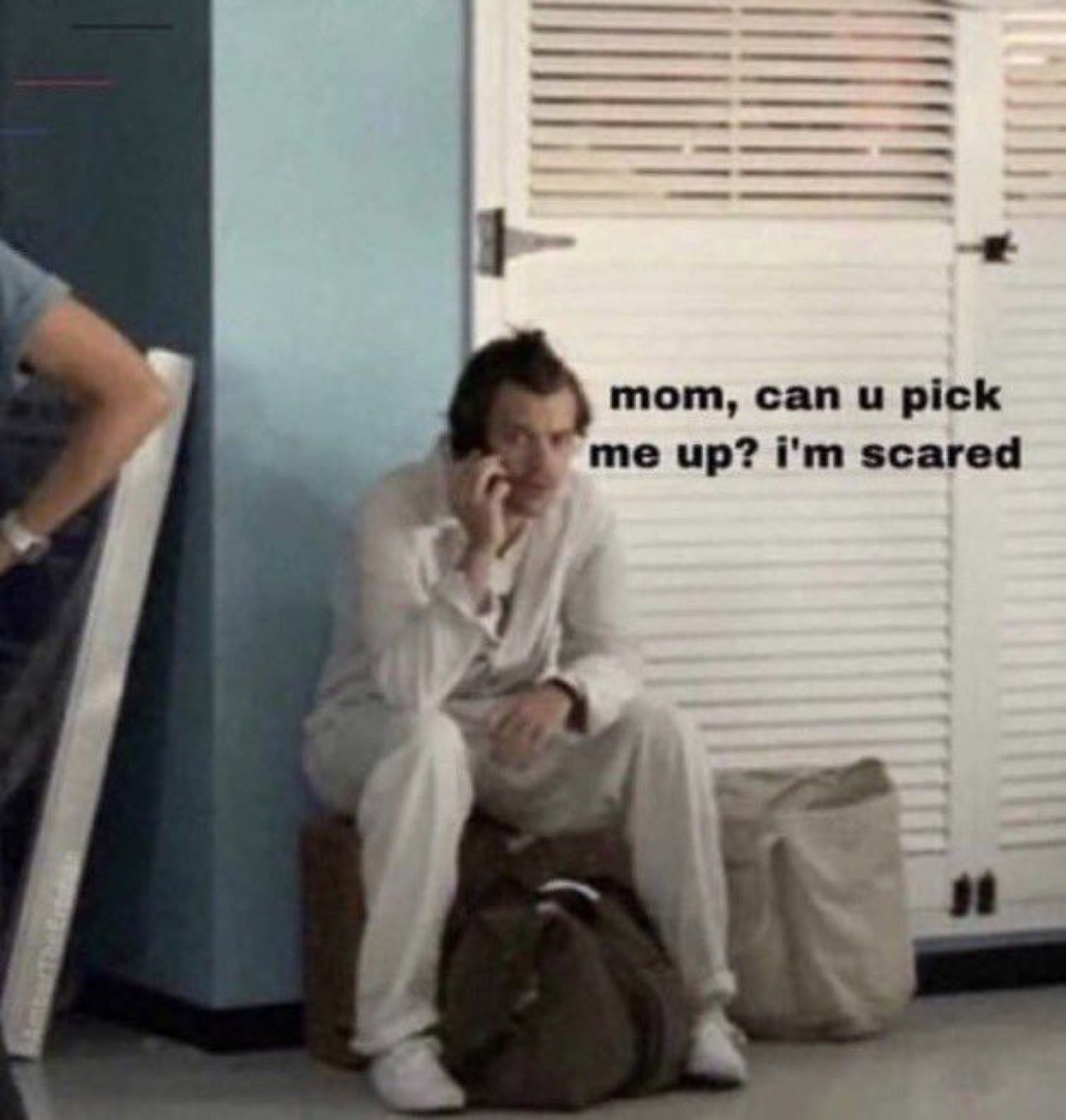 Man sitting on luggage on the phone, captioned 'mom, can u pick me up? i'm scared'