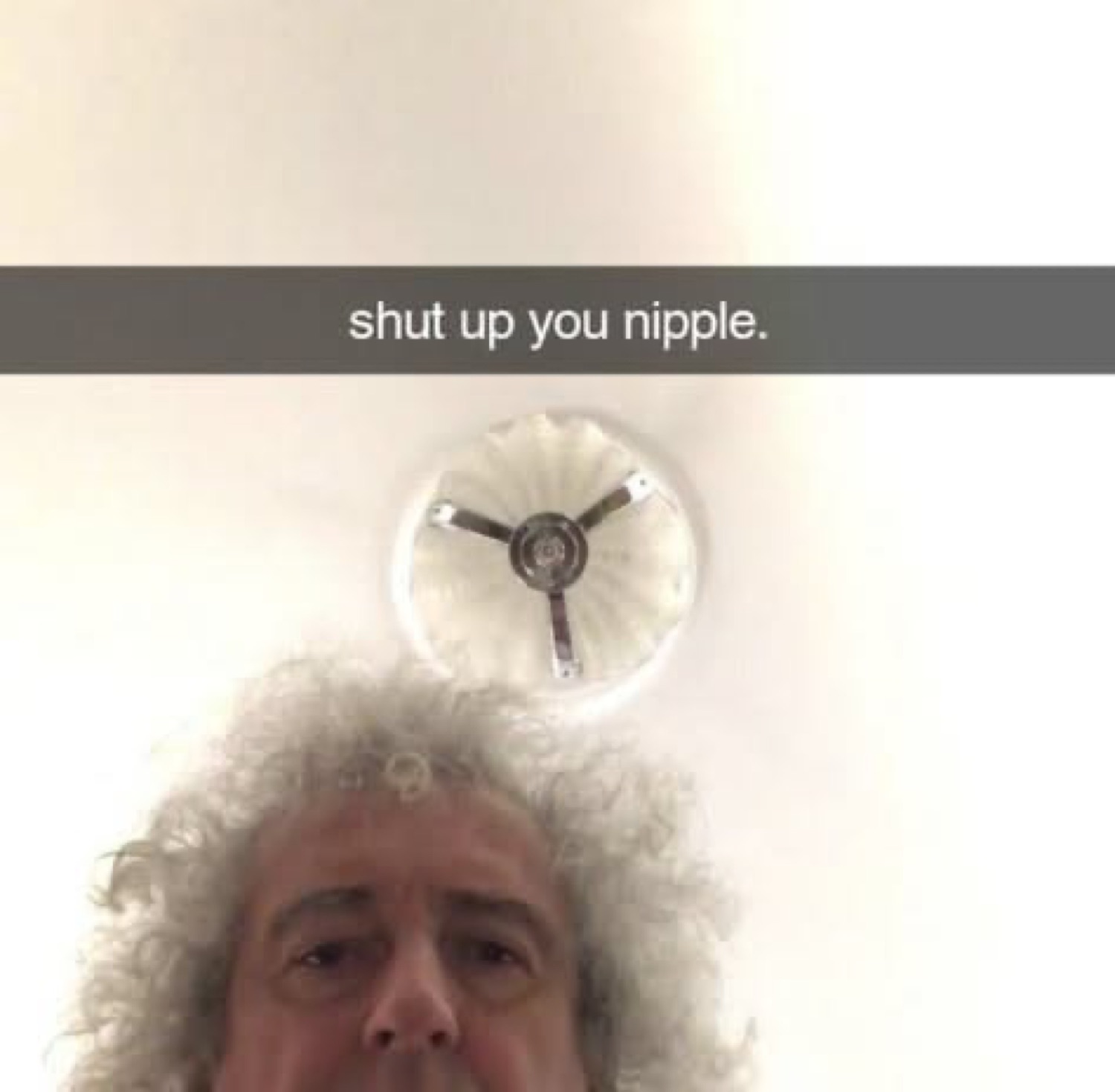 Curly-haired man peeking from the bottom of a ceiling selfie captioned 'shut up you nipple.'