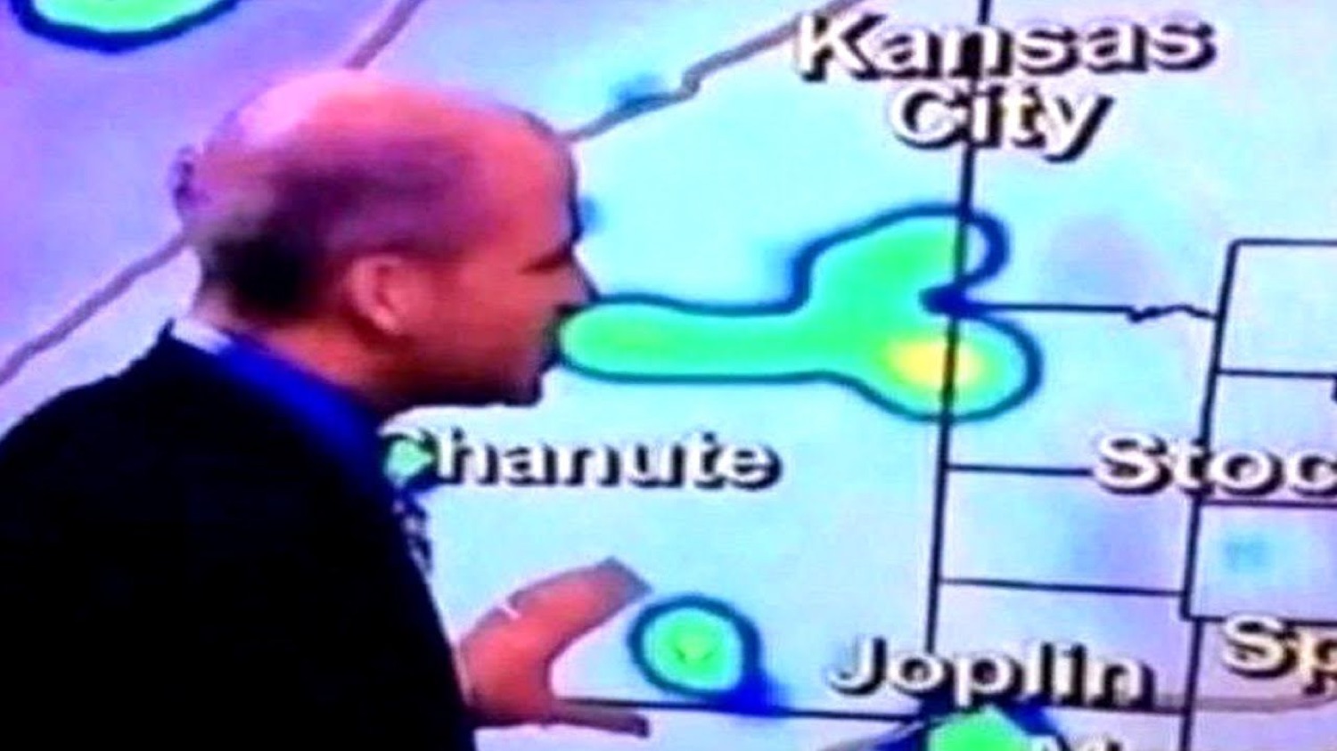 Weatherman standing in profile in front of a green radar blob over a Kansas map