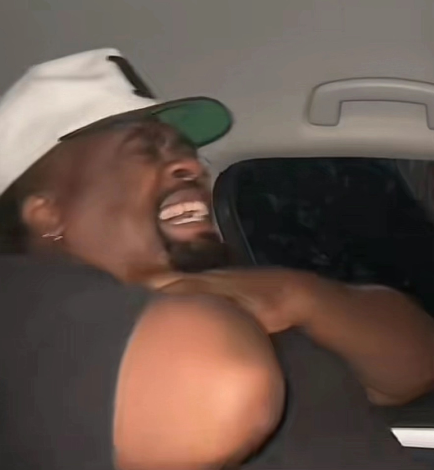 Guy in a car seat wearing a cap leaning back and absolutely losing it with uncontrollable laughter